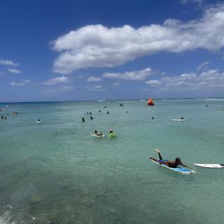 A vibrant day at the beach with surfers enjoying the clear waters under a bright blue sky.
