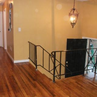 A hallway with wooden flooring, featuring a staircase with metal railings and a decorative lighting fixture.