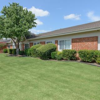 A well-maintained building with a lush green lawn and neatly trimmed bushes under a partly cloudy sky.
