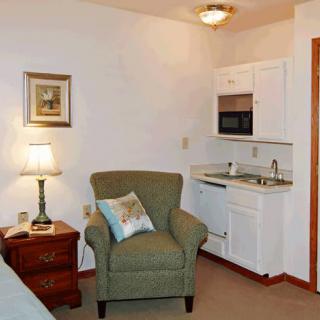 A cozy living space with a chair, lamp, and small kitchen area.