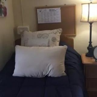 A cozy bedroom with a neatly made bed, pillows, a lamp, and a calendar on the wall.
