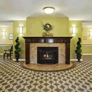 A warmly decorated lobby featuring a central fireplace with surrounding plants and patterned carpet.