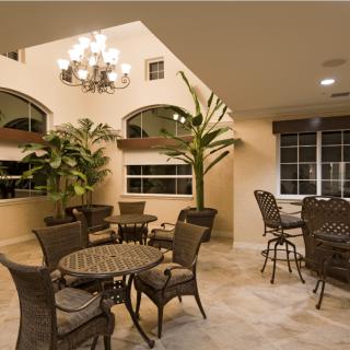 A cozy indoor dining area with wicker furniture, large plants, and a chandelier.