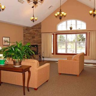 A cozy living room featuring sofas, a large window with curtains, a wooden table with a plant, and elegant chandeliers.