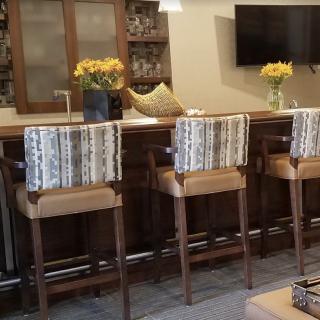 A cozy bar area featuring wooden stools, a countertop with flowers, and a television mounted on the wall.
