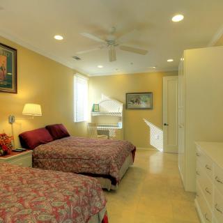 A cozy bedroom with twin beds, featuring a ceiling fan, artwork on the walls, and a window allowing natural light.