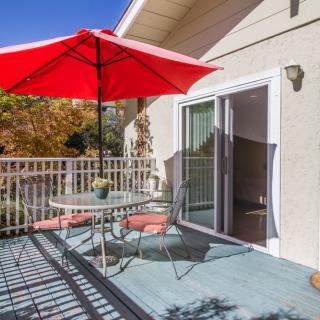 A sunny patio with a red umbrella, table, and chairs.