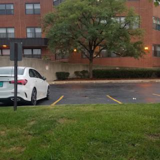 A white car parked in front of an apartment building, surrounded by green grass and a tree.