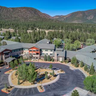 Aerial view of a hotel nestled in a forested area with mountains in the background.