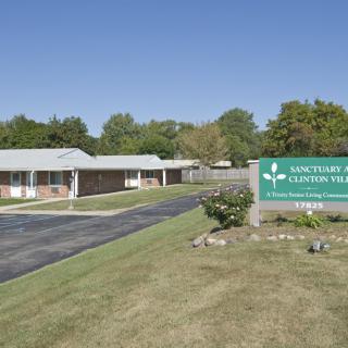 A view of a nursing home with a sign and driveway surrounded by trees.