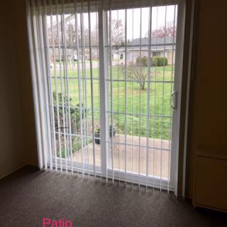A room with a sliding glass door and vertical blinds, overlooking a patio and grassy yard.