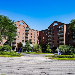 A brick apartment building surrounded by trees and landscaping under a clear blue sky.