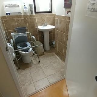 A view of a small accessible bathroom featuring a toilet, sink, and tiled walls.