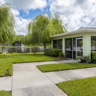 A modern house with a green lawn and driveway, situated next to a lake under a cloudy sky.