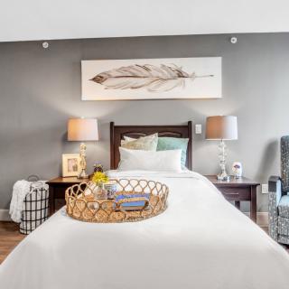A cozy bedroom featuring a neatly made bed with a decorative tray, flanked by lamps on wooden nightstands and adorned with wall art.