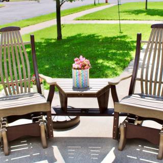 Two rocking chairs and a table with a flower arrangement on a sunny patio.