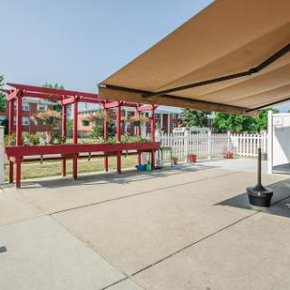 A spacious outdoor patio featuring a red wooden structure, an awning for shade, and a well-maintained garden area.