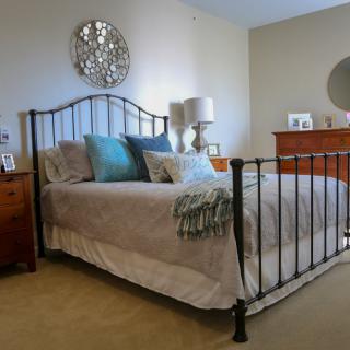 A well-decorated bedroom with a metal bedframe, colorful pillows, and wooden furniture.