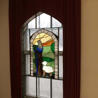 A stained glass window depicting a shepherd with sheep against a scenic background.