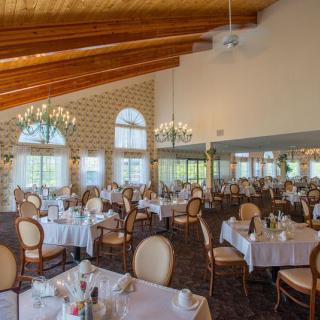 An elegant restaurant dining room with neatly arranged tables and chairs, large windows, and decorative chandeliers.
