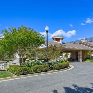 A scenic view of a building surrounded by a landscaped garden and driveway under a clear blue sky.