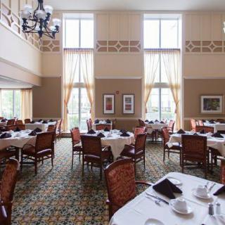 An elegant dining room with neatly arranged tables and chairs, featuring large windows and a chandelier.