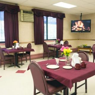 A cozy dining area with neatly arranged tables and a television displaying a fireplace.