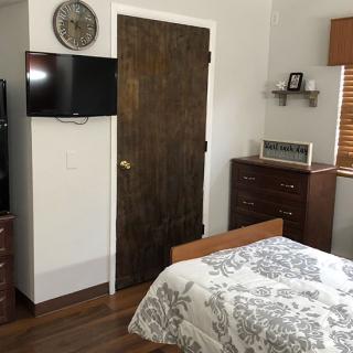 A cozy bedroom with a television mounted on the wall, wooden furniture, and a neatly made bed.