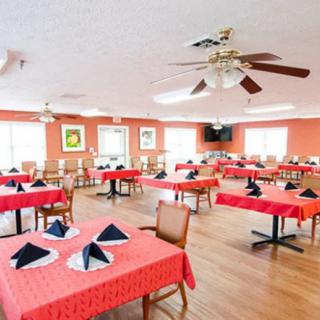 An empty dining room with red tablecloths and neatly arranged tables, featuring ceiling fans and casual decor.