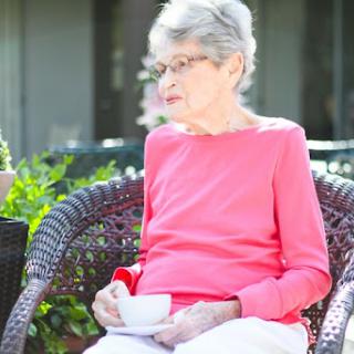 An elderly woman enjoying a quiet moment with a cup of tea in a serene outdoor setting.