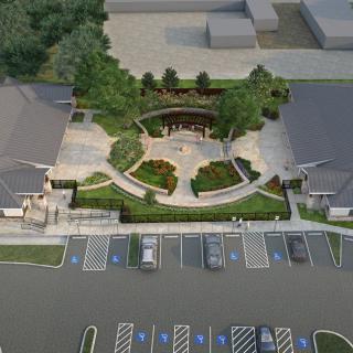 Aerial view of a landscaped area with pathways and greenery, adjacent to a parking lot.