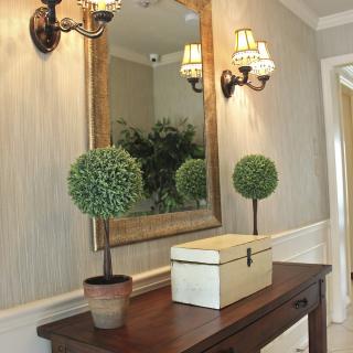 A stylish hallway features a wooden console table, decorative potted plants, and an ornate mirror with elegant wall sconces.