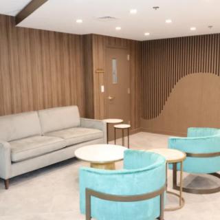A modern lounge area featuring a sofa, turquoise chairs, and round tables with elegant wood paneling.