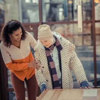 A young woman assists an elderly lady indoors, providing care and support.