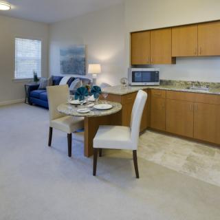 A modern apartment with an open kitchen and dining area, featuring wooden cabinets and a small dining table.