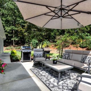 A cozy outdoor patio with comfortable seating, a large umbrella, and a grill, surrounded by lush greenery.