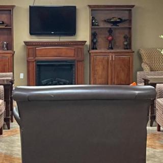 A cozy living room with a TV mounted above a fireplace, surrounded by shelves and seating.