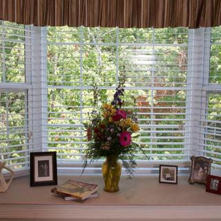A window sill adorned with a vase of colorful flowers and framed pictures, overlooking a lush green view.