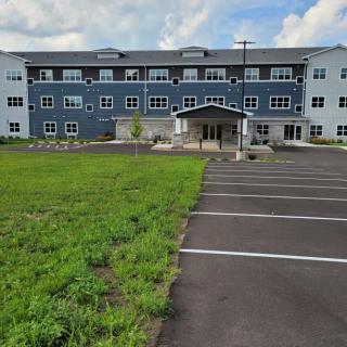 A modern residential building with a parking lot and grassy area in front.