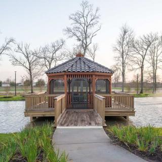 A wooden gazebo situated on a small lake, connected by a walkway amidst trees and serene nature.