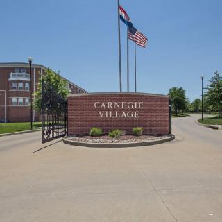 Entrance sign for Carnegie Village with flags displayed above.