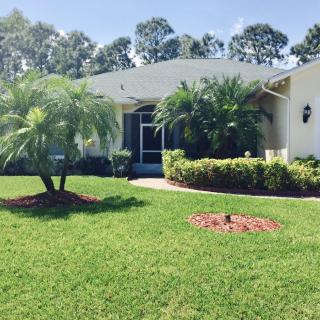 A suburban house with a well-manicured lawn and palm trees in the front yard on a sunny day.