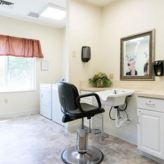 A clean and bright hair salon interior with a barber chair, mirror, and sink.