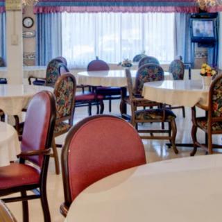 A well-lit dining room with tables and chairs arranged neatly near large windows with curtains.