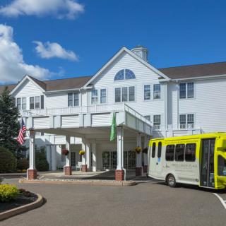 A white building with a front entrance and a yellow bus parked nearby.