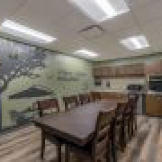 A kitchen with a large wooden dining table and chairs, featuring a wall mural and wood flooring.