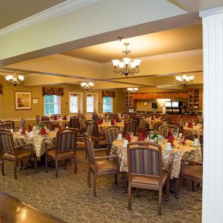 An elegantly decorated dining room with arranged tables and chairs, illuminated by chandeliers.