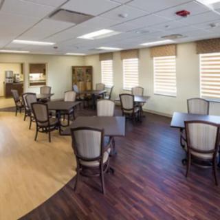 An empty dining area with wooden tables and chairs, well-lit by ceiling lights and natural light from the windows.