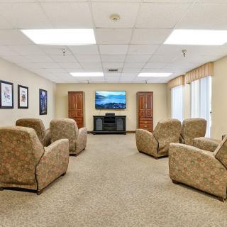 A cozy living room with multiple recliners facing a television, framed artwork on the walls, and ample natural lighting.