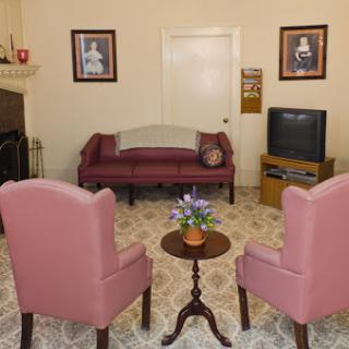 A cozy living room setup featuring a sofa, two pink armchairs, and a small coffee table with flowers.